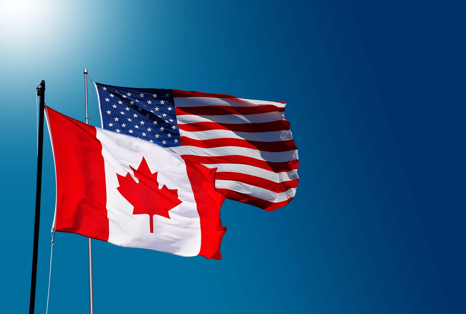Canadian flag and American flag over a blue sky