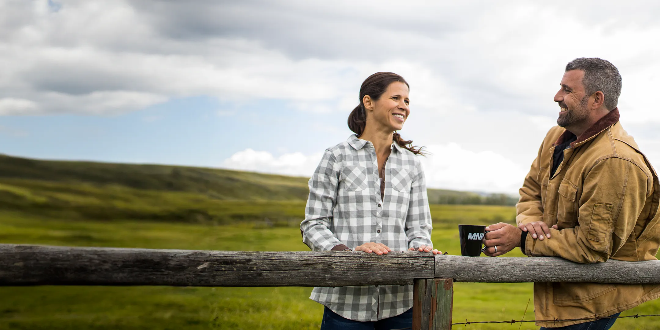 Man and woman leaning on a fence talking in front of a large field