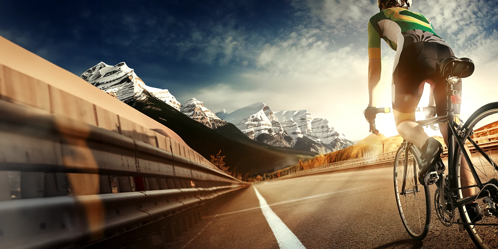 Man riding a bicycle on the road with mountains in the background.