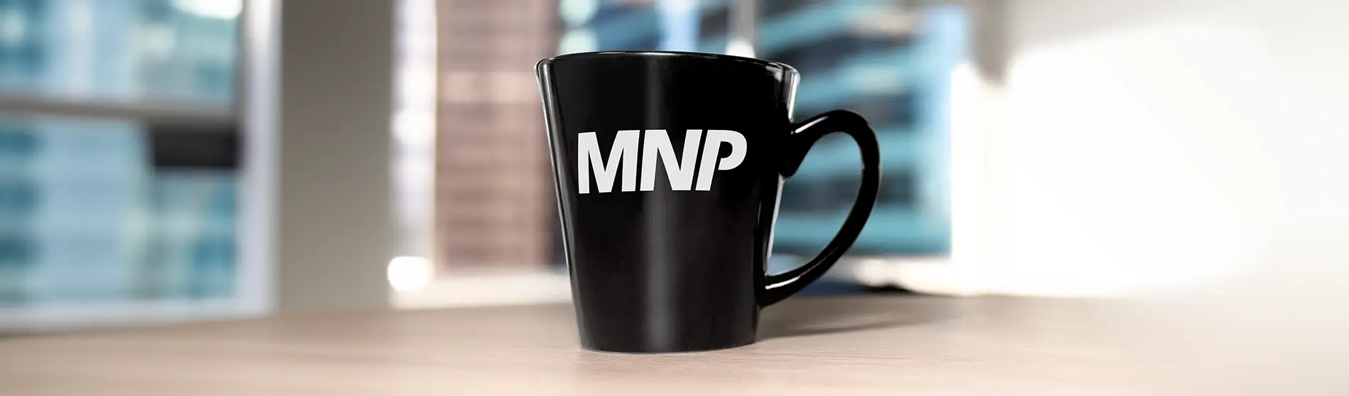 MNP branded black mug with blurred background of an office.