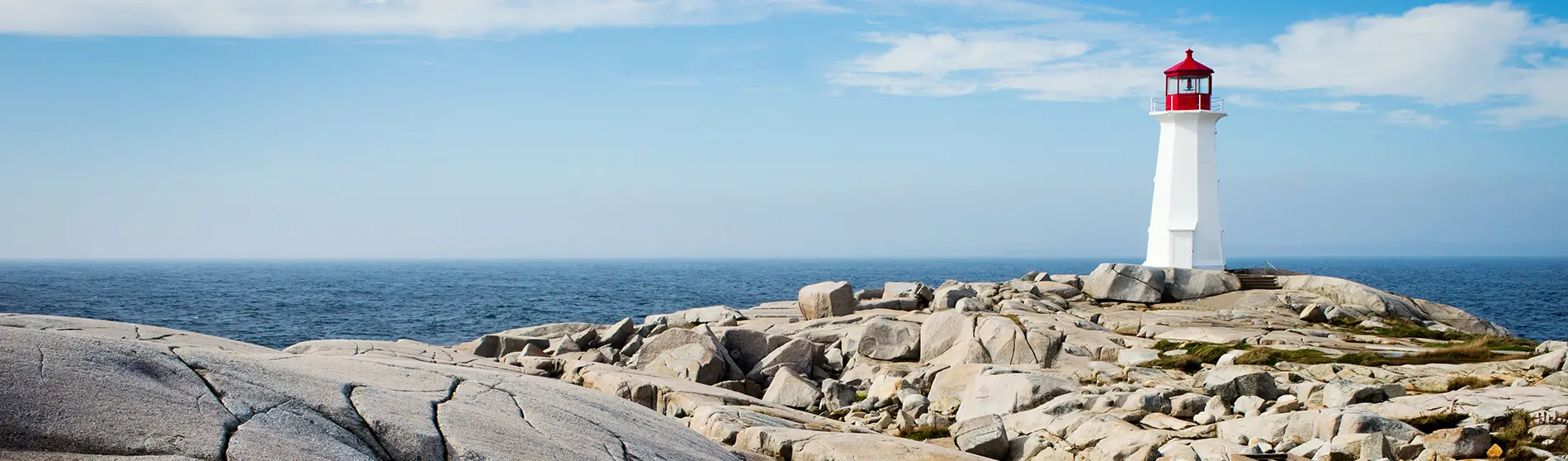 Peggys Point Lighthouse in Nova Scotia Canada with blue sky and rocks in foreground