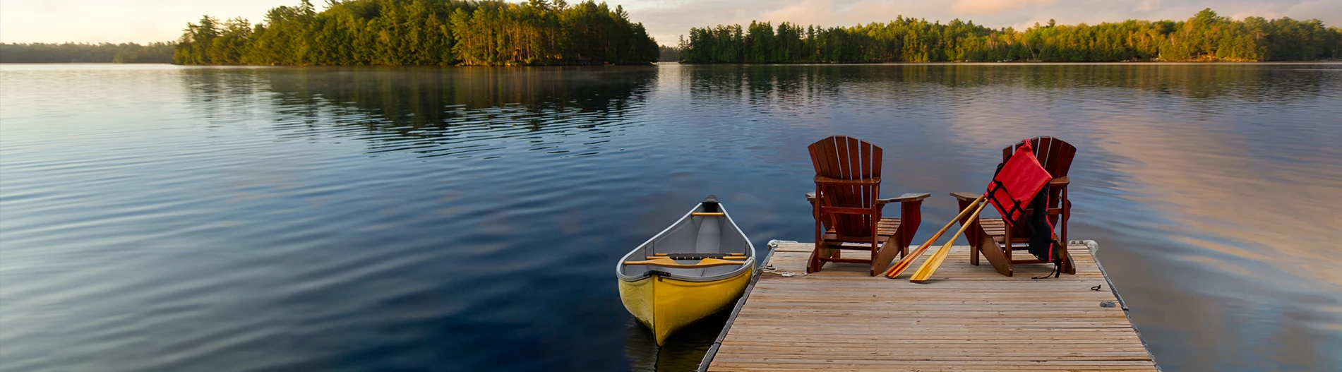 Two Adirondack chairs on a wooden dock overlooking a calm lake