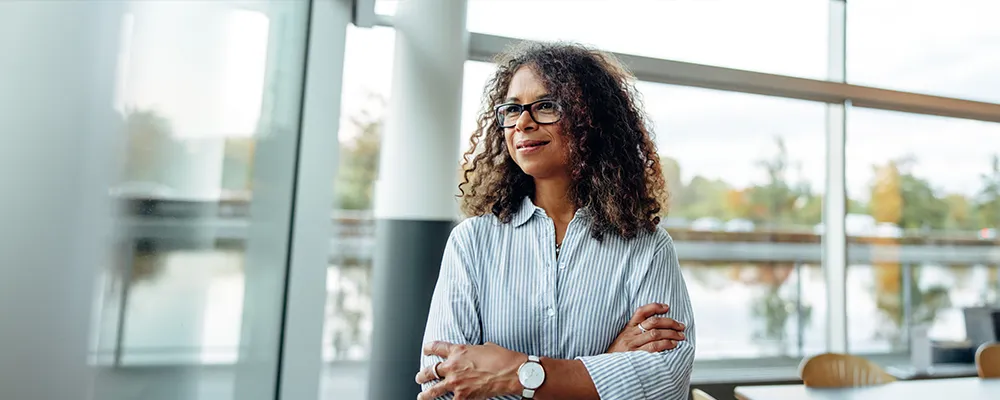 Older woman with curly hair smiling with arms folded 