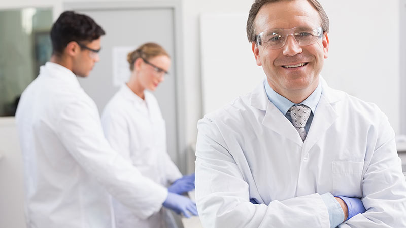 Three people wearing white jackets, blue gloves and safety goggles