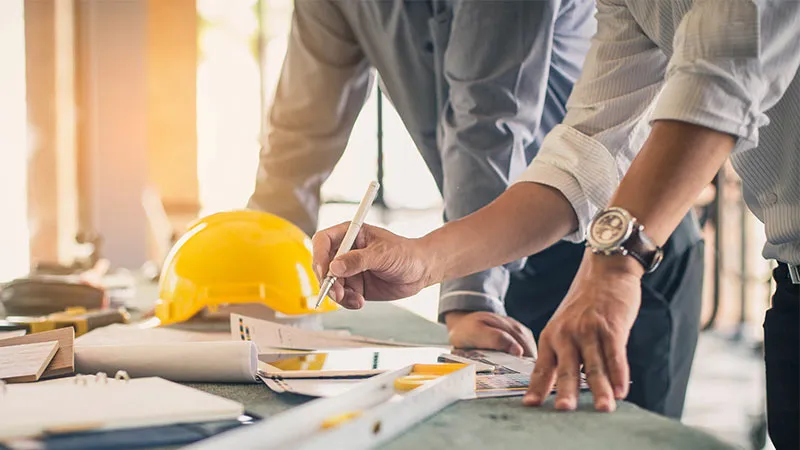 Gros plan sur deux personnes travaillant à un bureau de construction plein d'outils, de plans et d'un casque jaune