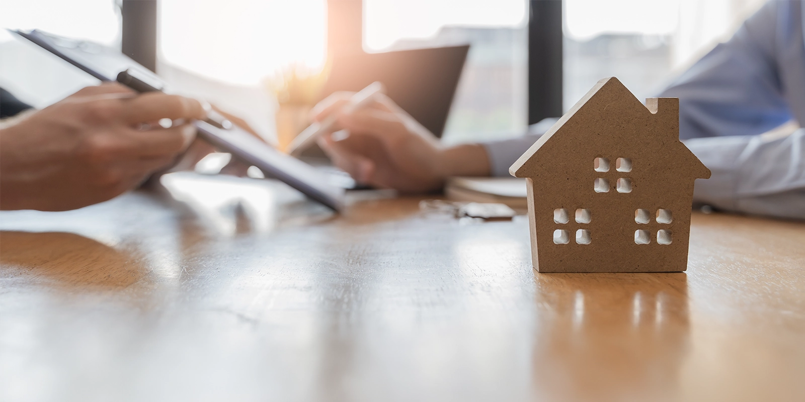 Real estate agent and client signing papers in background, miniature house in the foreground 