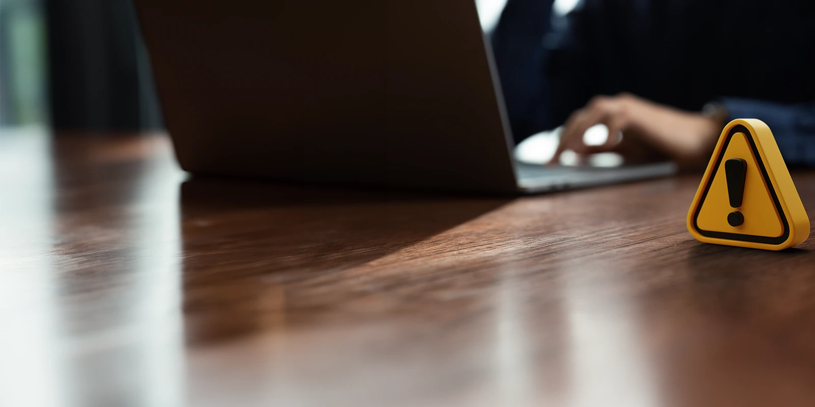 Warning sign on table in front of individual working on a laptop