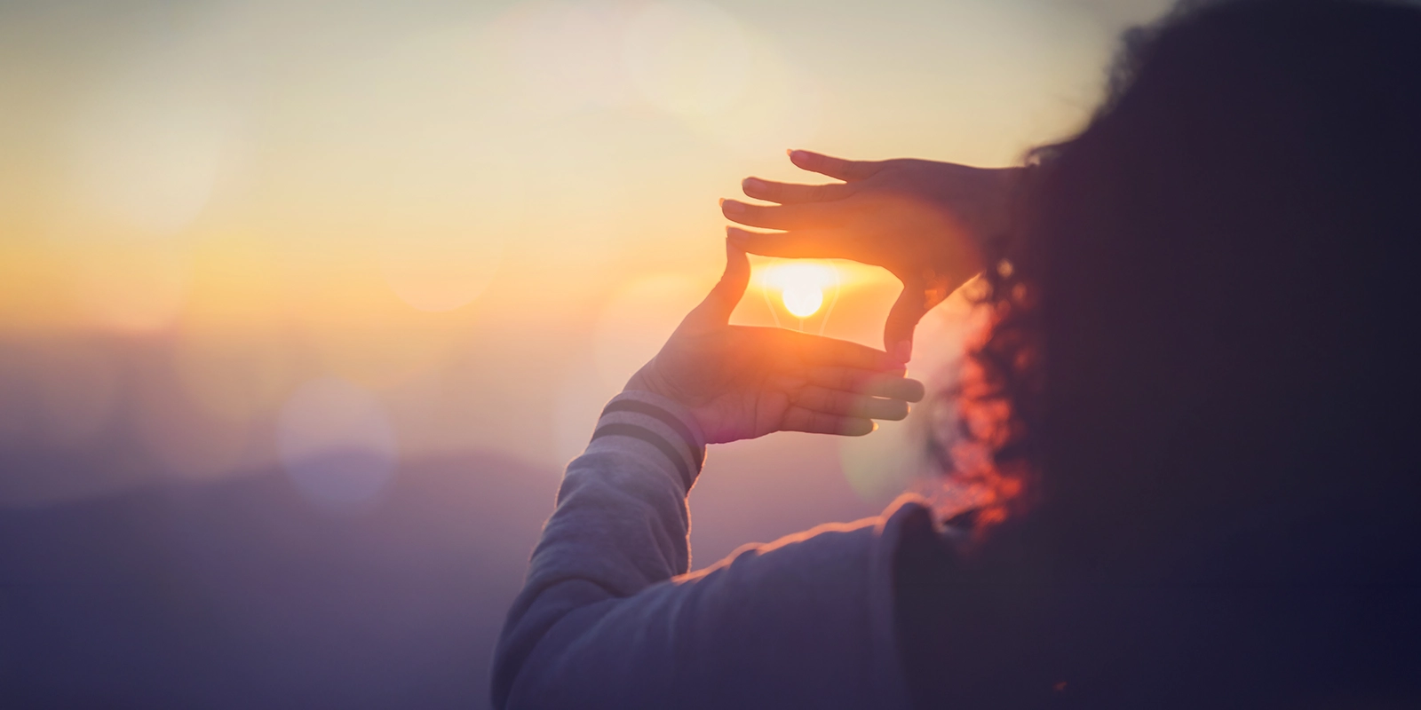 Personne faisant un cadre avec ses mains autour du soleil.