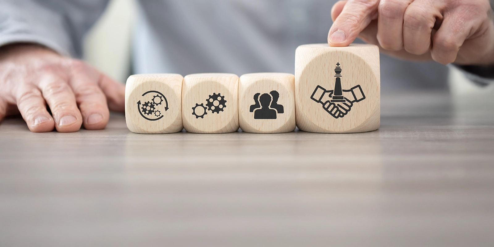 Person's hand pointing to a wooden block with business related symbols on them.