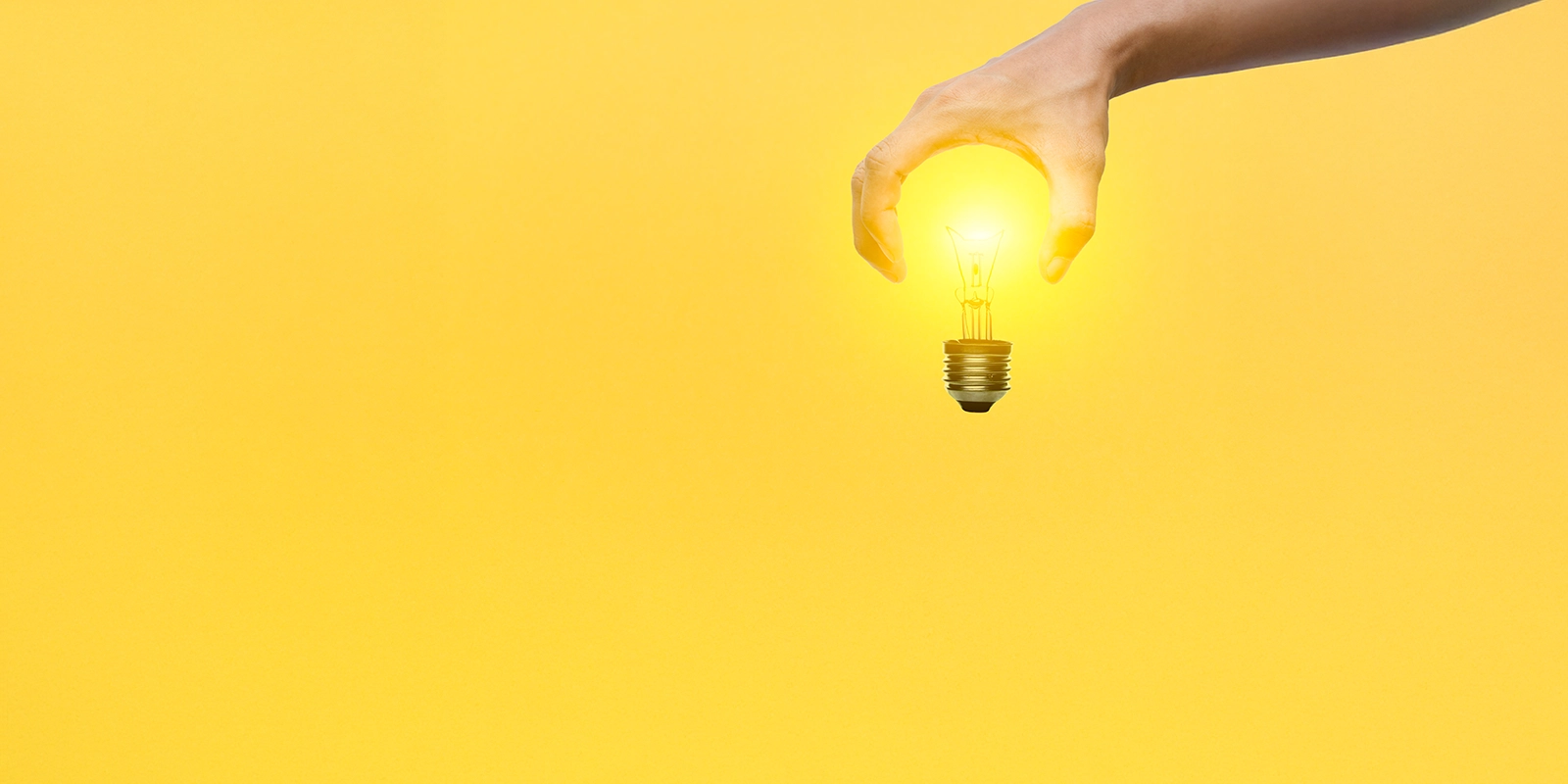 Hand holding a light bulb that's turned on on a yellow background.