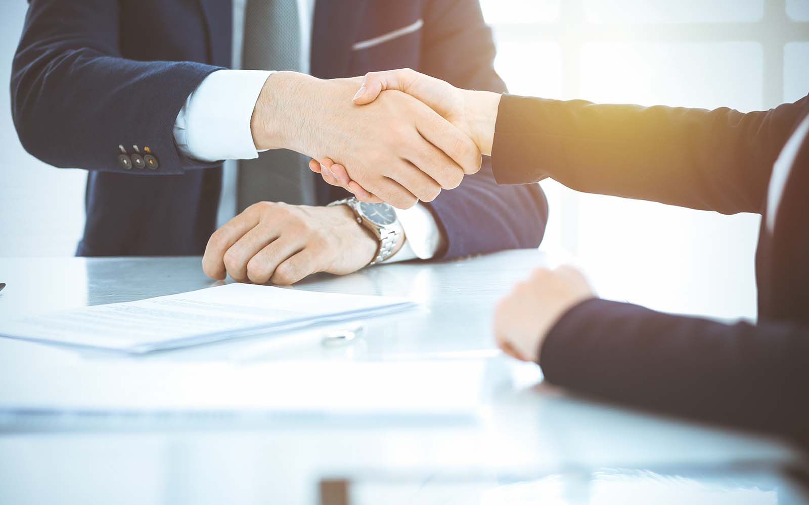 Des hommes d'affaires se serrant la main pour terminer une réunion ou une négociation dans un bureau ensoleillé.